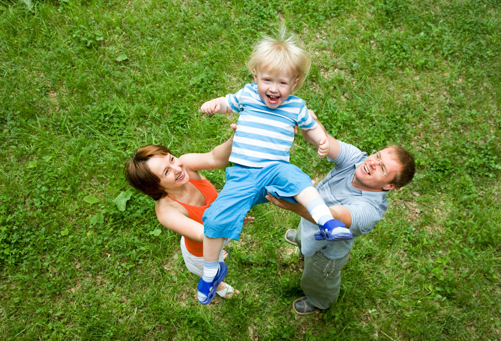 child playing in the grass with parents